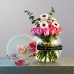 A rounded glass vase filled with soft pink roses and white and peach gerbera daisies, accented with fresh eucalyptus greenery.