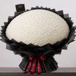 A large bouquet of elegant white roses arranged in a full, rounded shape, wrapped in sophisticated black paper and finished with a refined ribbon.