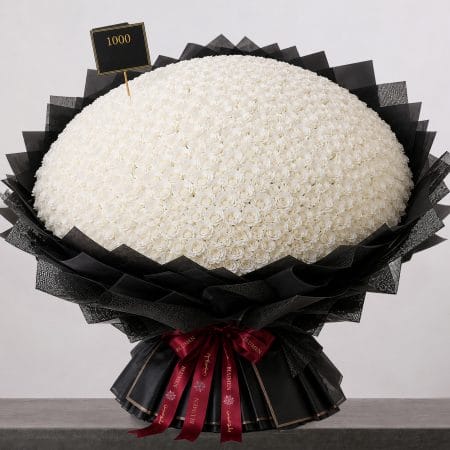 A large bouquet of elegant white roses arranged in a full, rounded shape, wrapped in sophisticated black paper and finished with a refined ribbon.