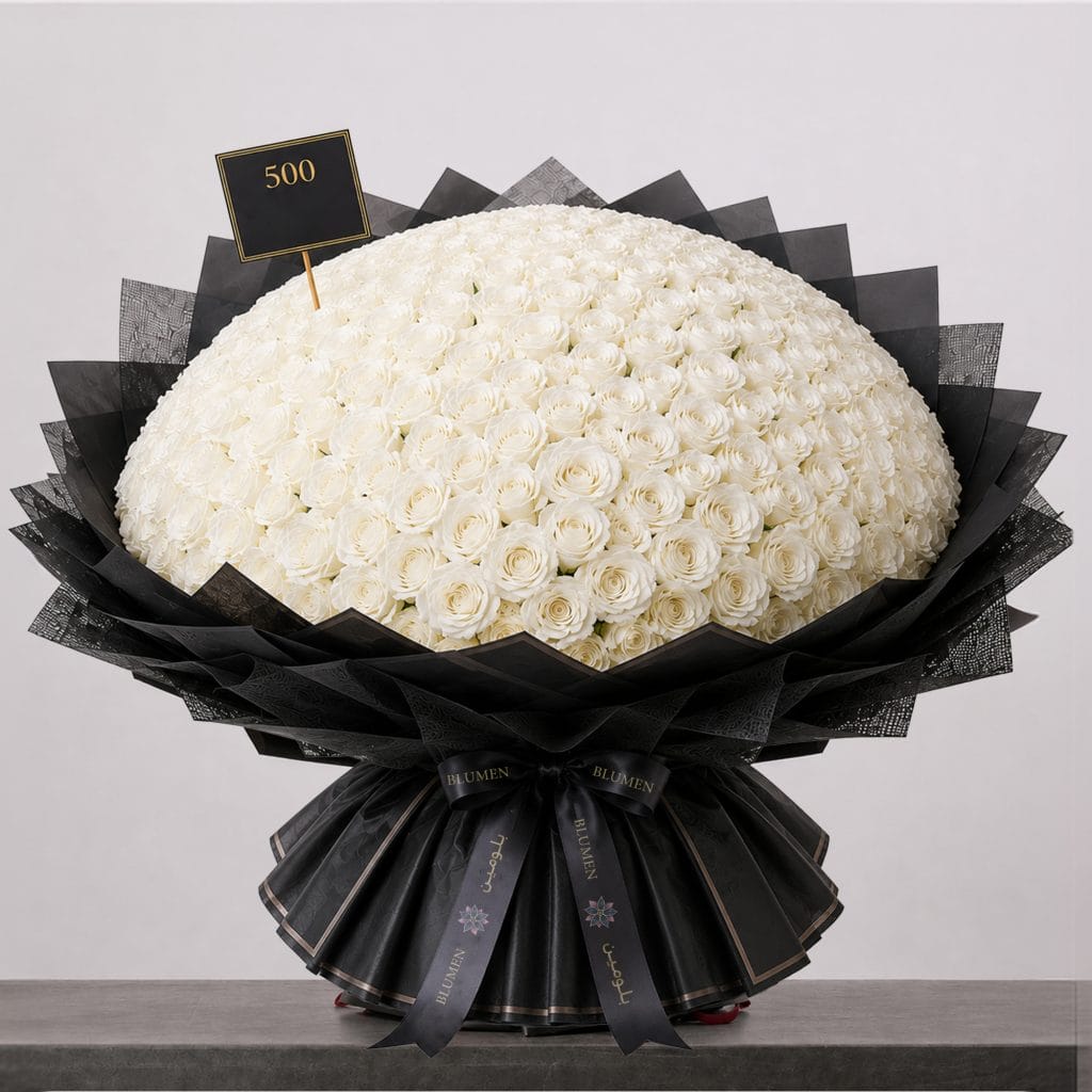 A large bouquet of elegant white roses arranged in a full, rounded shape, wrapped in sophisticated black paper and finished with a refined ribbon.