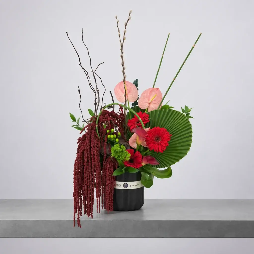 Rouge Atelier luxury floral arrangement featuring pink anthuriums, red gerbera daisies, cascading burgundy amaranthus and sculptural greenery in an elegant black vase by Blumen.