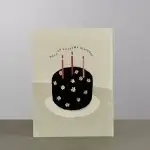 A beige card holder with a black cake wishing a happy birthday.