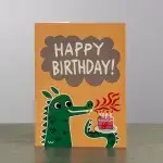 A card holder with the image of a green dinosaur breathing fire onto the candles on the birthday cake.