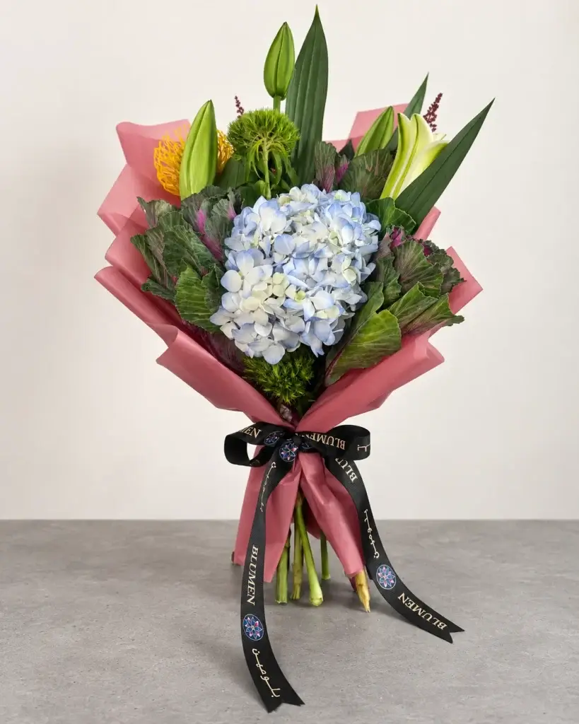 Jardin Bleu luxury flower bouquet featuring blue hydrangea, white lilies, exotic blooms and lush greenery, wrapped in dusty pink paper with Blumen’s signature black ribbon.